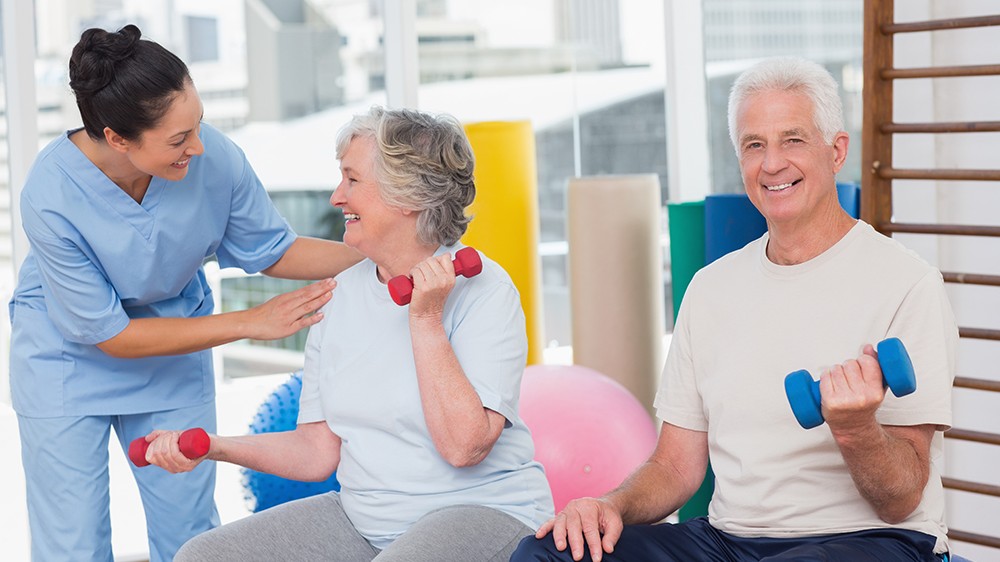 Happy trainer communicating with senior woman sitting by man in gym