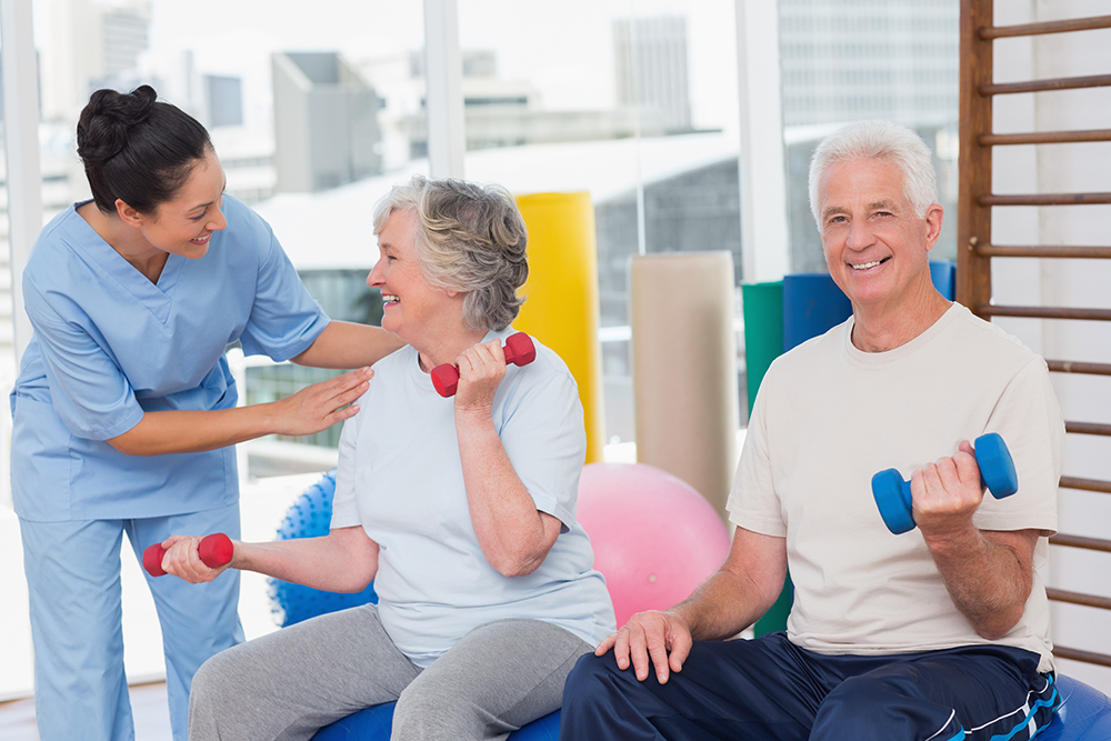 Happy trainer communicating with senior woman sitting by man in gym